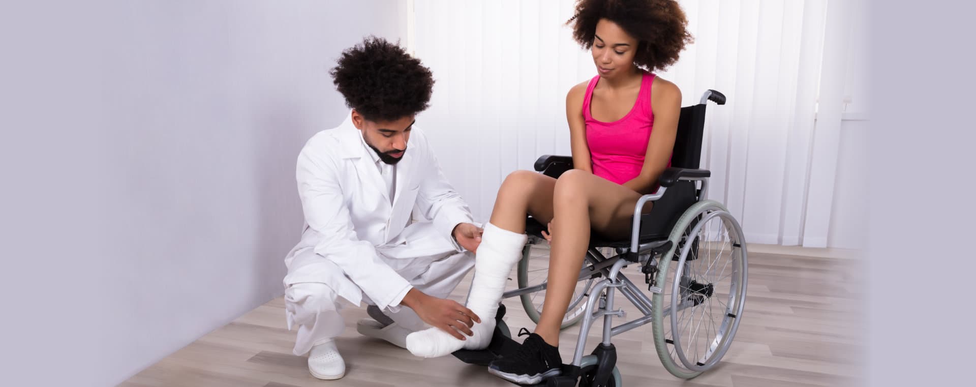 Male Physiotherapist Examining Leg Of Female Patient Sitting On Wheelchair