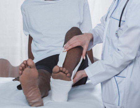 Doctor putting on plaster cast on injured african american patient leg in the clinic